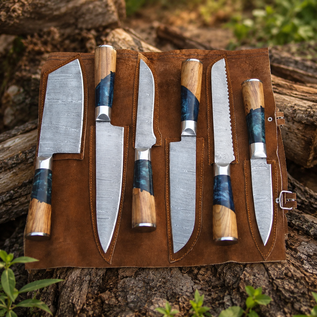 7-piece handmade kitchen knife set with patterned blades, wood and blue resin handles, and brown leather roll bag on natural log background
